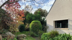 Une maison dotée d’un jardin bien entretenu, comprenant une pelouse, des rochers et divers arbustes.
