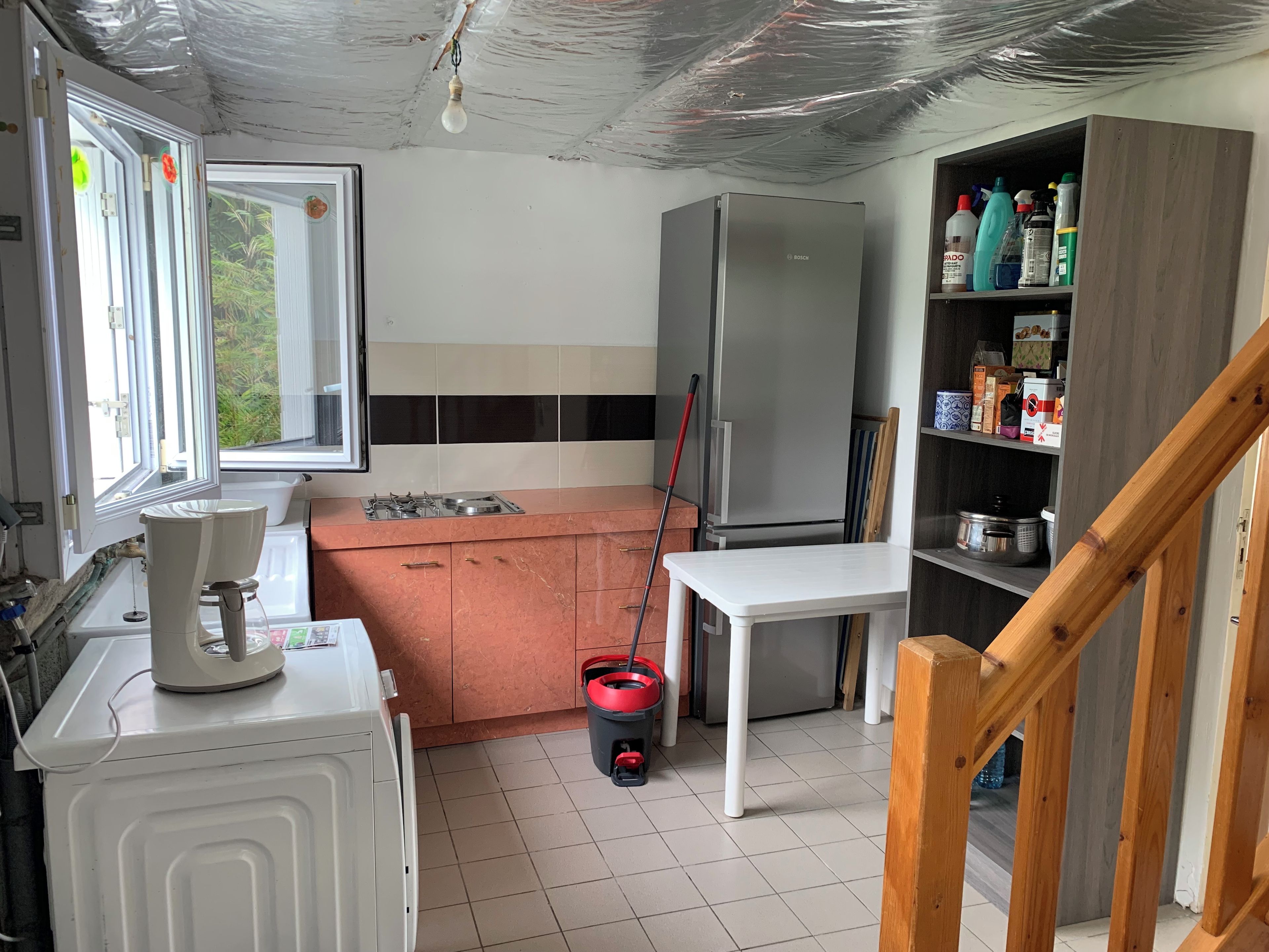 Kompakti keittiö, jossa on Bosch-merkkinen jääkaappi, pesuallas, liesi ja ikkuna, jossa on verhot.