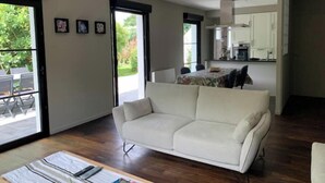 Un salon moderne avec un canapé blanc, une table à manger et un coin cuisine visible à travers une porte ouverte.