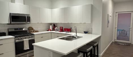 Una cocina moderna con armarios blancos, una isla central con taburetes, un lavamanos de acero inoxidable y un microondas.