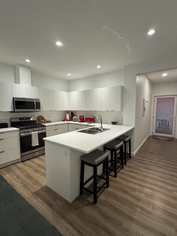 Una cocina moderna con armarios blancos, una isla central con taburetes, un lavamanos de acero inoxidable y un microondas.