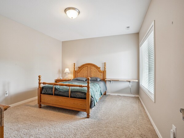 A bedroom with a wooden bed, a nightstand, a lamp, and a window with blinds. - 300 on Abigail.
4BR/3BA. Large kitchen. Deck with TV. Playground. (Waukee)