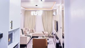 A modern living room with a sofa, coffee table, and a TV mounted on the wall. - Purple Lavender Court Apartment (Lagos)