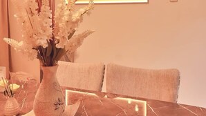 A dining table with a vase of flowers, a modern wall art piece, and a light switch on the wall. - Purple Lavender Court Apartment (Lagos)