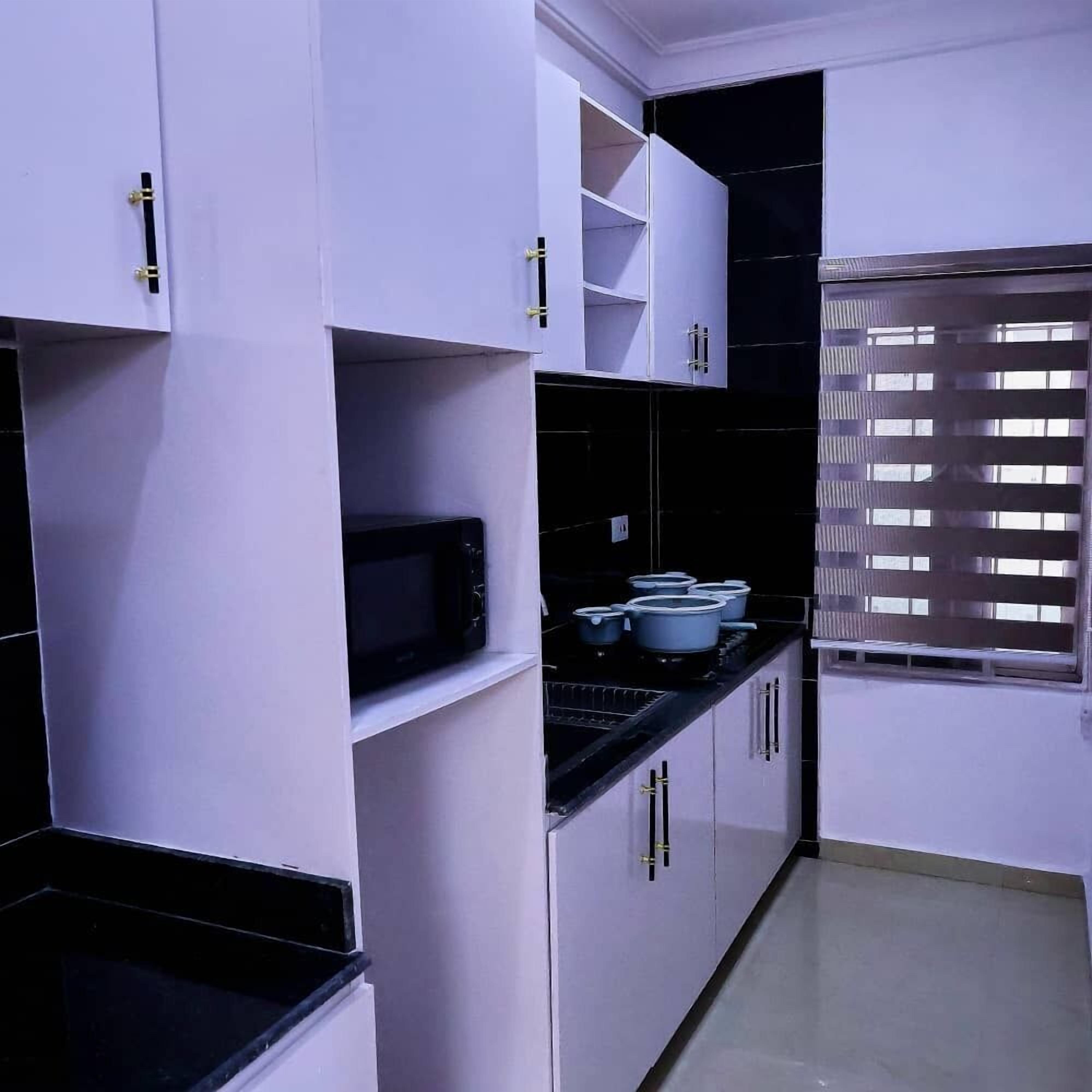 A kitchen with white cabinets, a black countertop, and a window with blinds.