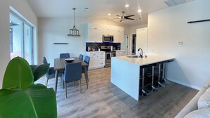 Une cuisine moderne avec des meubles blancs, un îlot central et un coin repas avec des chaises bleues.