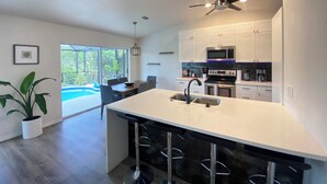 Une cuisine moderne avec des meubles blancs, un îlot central doté d’un évier et un ventilateur de plafond.