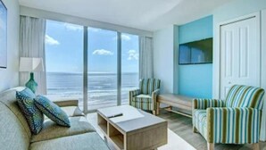 Ein modernes Wohnzimmer mit einem großen Fenster und Meerblick, einer Couch, einem Couchtisch und gestreiften Sesseln.