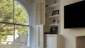 Huoneen nurkassa on suuri ikkuna, valkoinen hyllykaappi ja seinälle asennettu taulutelevisio.