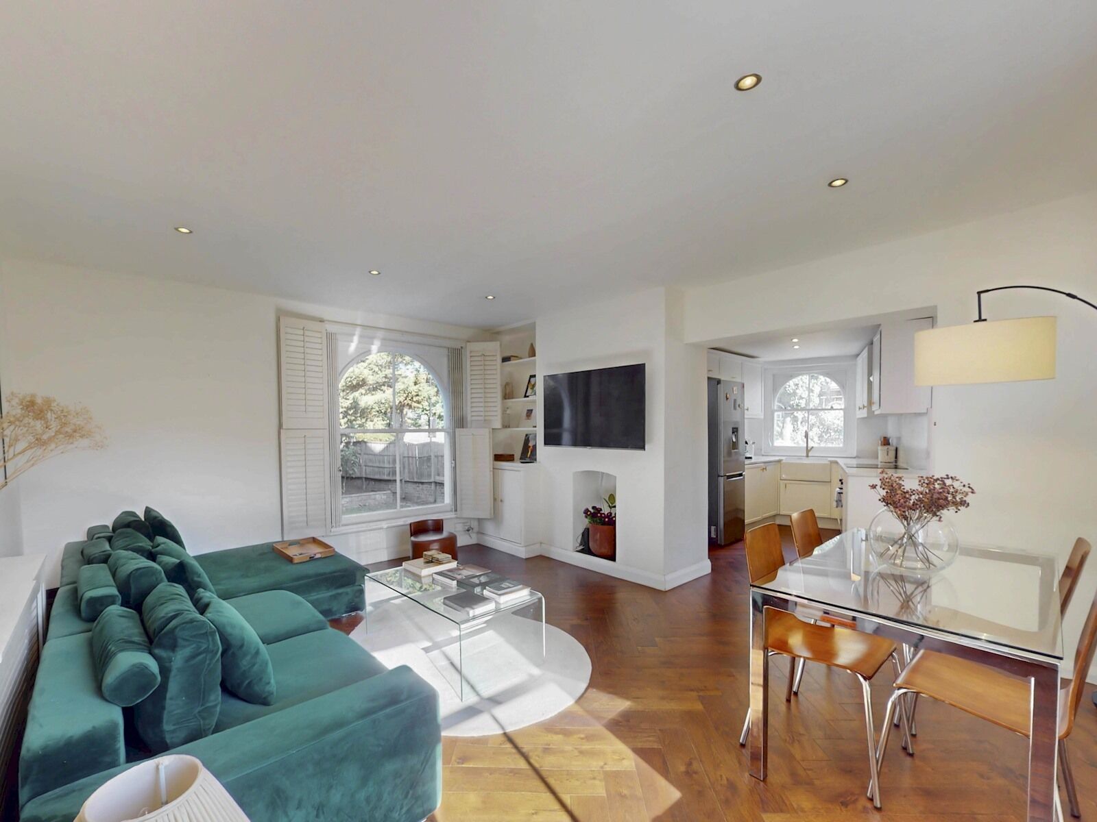 A modern living room with a green sofa, a glass coffee table, and a dining area with a glass table and chairs.