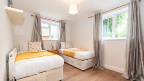 Une chambre double avec deux lits, un plancher en bois, une fenêtre avec des rideaux et un luminaire au plafond.