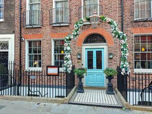 A brick building with a blue door, a black metal fence, and a decorative archway with flowers. - Stunning Modern Marylebone Flat, near to Hyde Park - Pass the Keys (London)