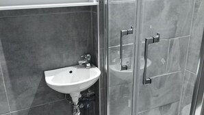 Un bany modern amb un espai de banyera de vidre, un lavabo blanc i un armari damunt del lavabo.