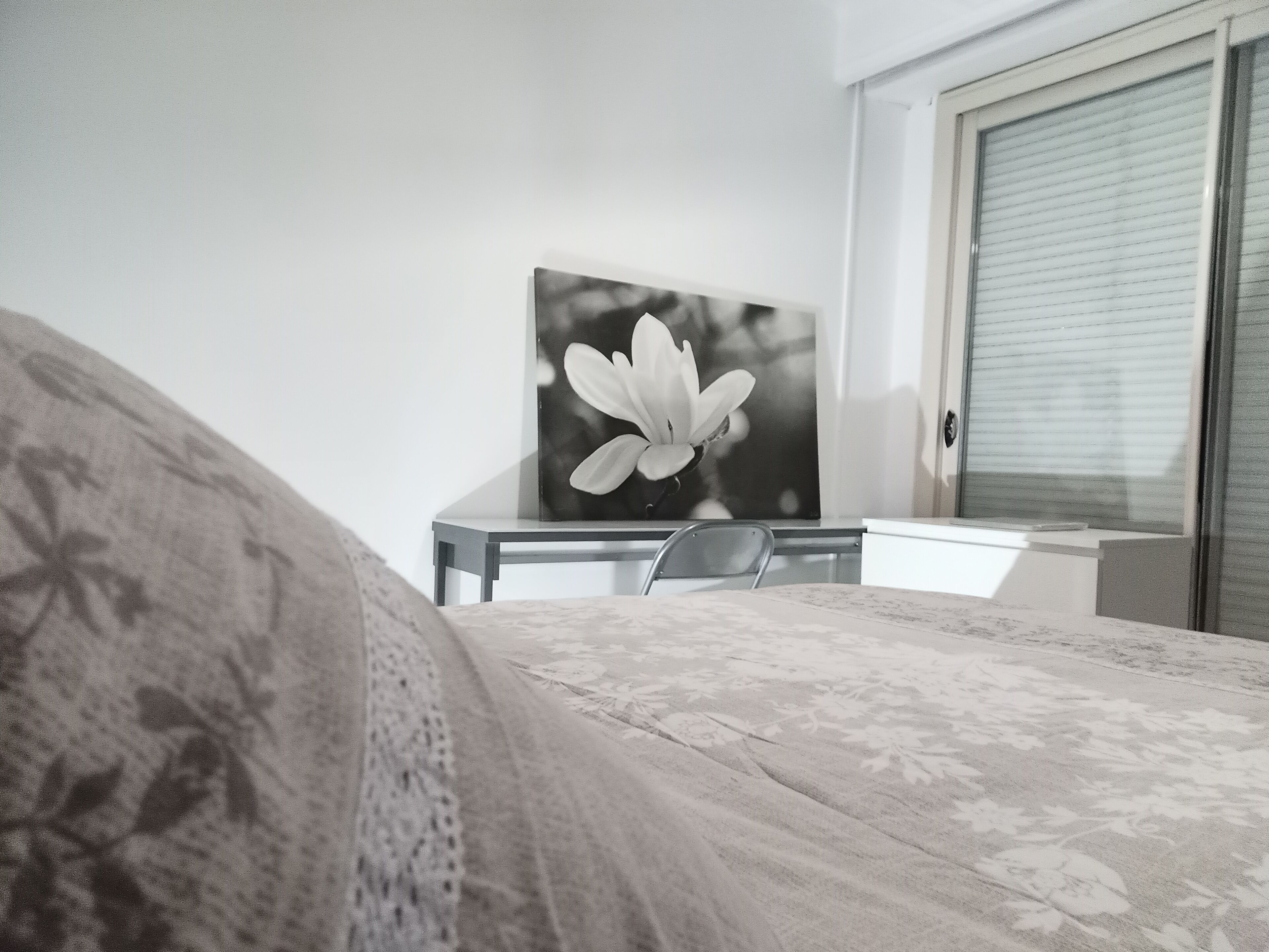Un dormitorio con una cama, un escritorio y una silla. Hay una ventana con persianas y una puerta.