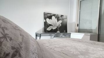 Un dormitorio con una cama, un escritorio y una silla. Hay una ventana con persianas y una puerta.
