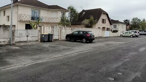 Un carrer residencial amb cases, un cotxe negre estacionat al costat i una furgoneta blanca al fons.