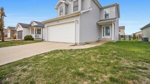 A two-story residential house with a garage, a front porch, and a well-maintained lawn. - Grey Moon Escape In Bloomington (Bloomington)