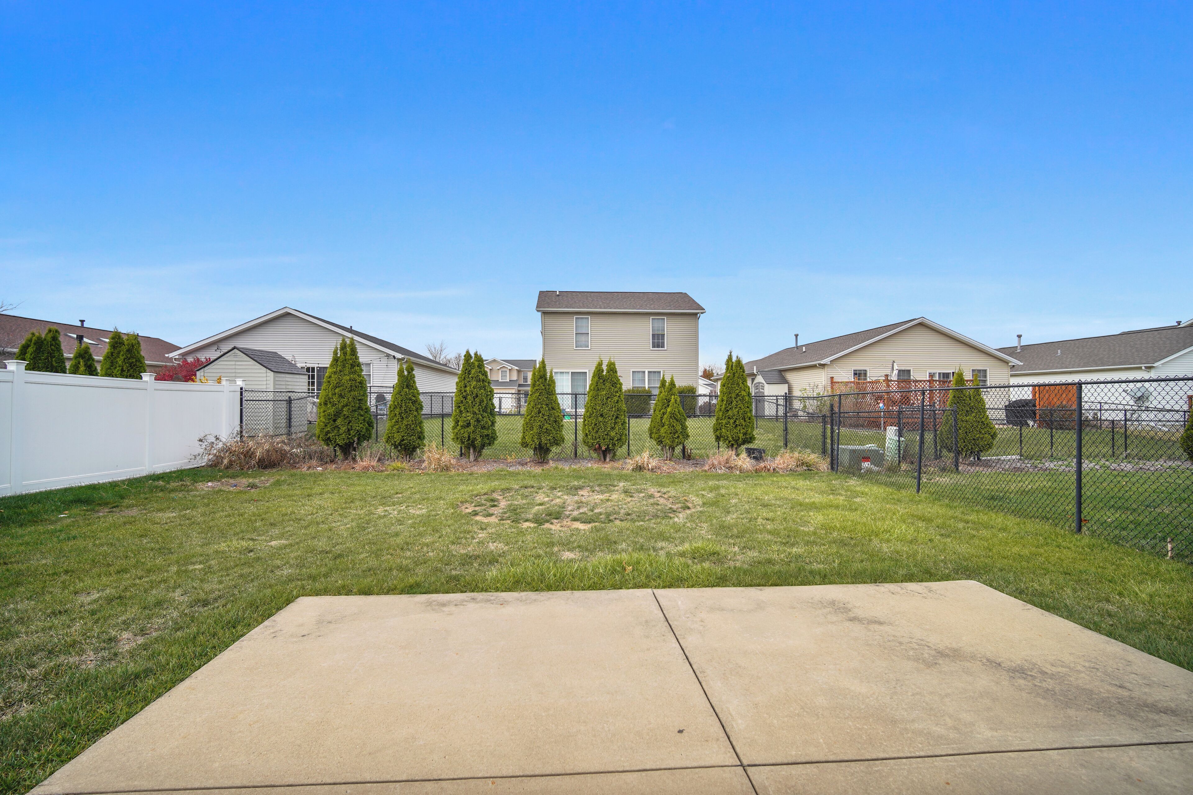 A residential area with houses, a fenced yard, and a concrete patio.