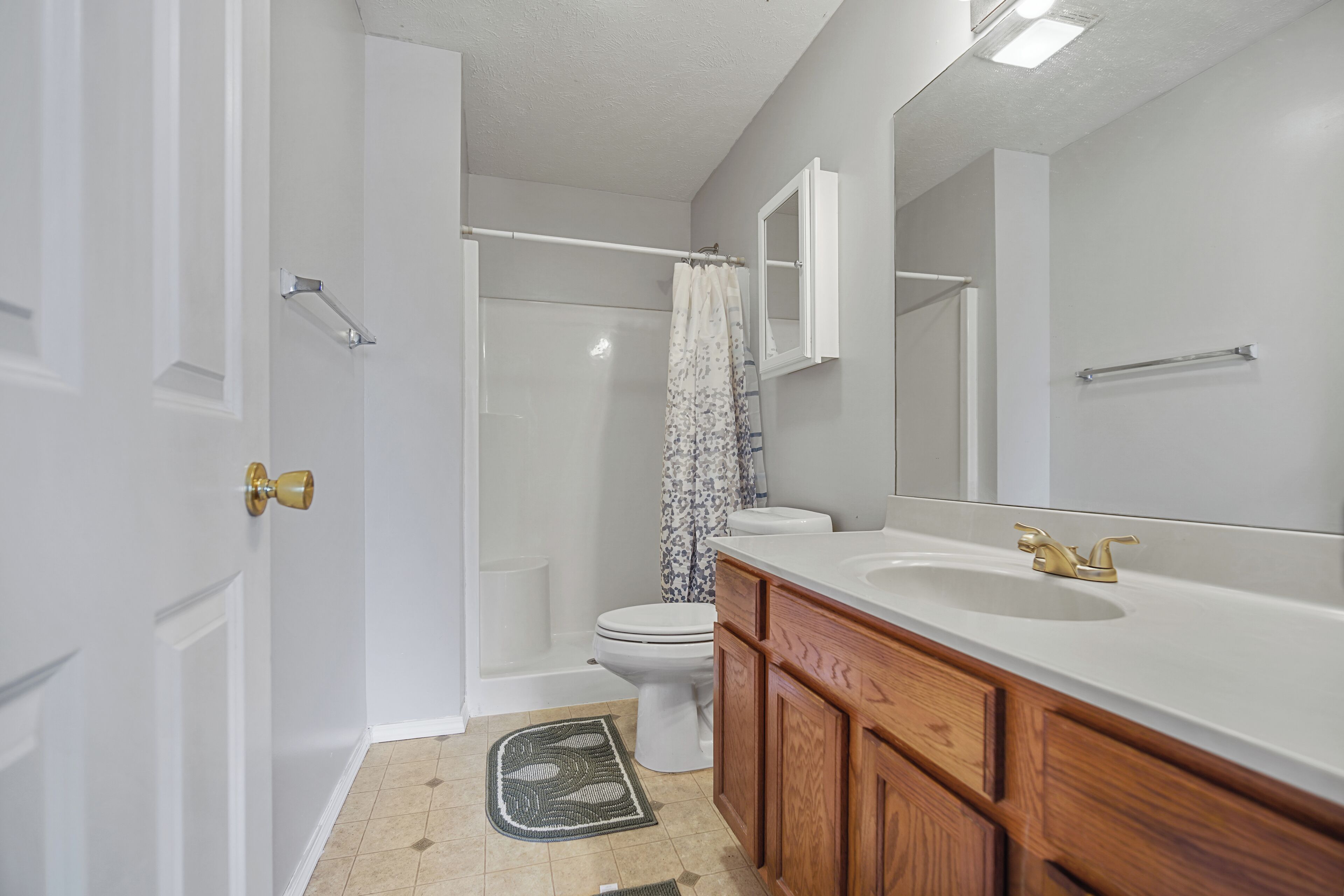 Un baño con inodoro blanco, ducha con cortina, un espejo grande y armarios de madera.