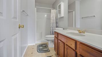 Un baño con inodoro blanco, ducha con cortina, un espejo grande y armarios de madera.