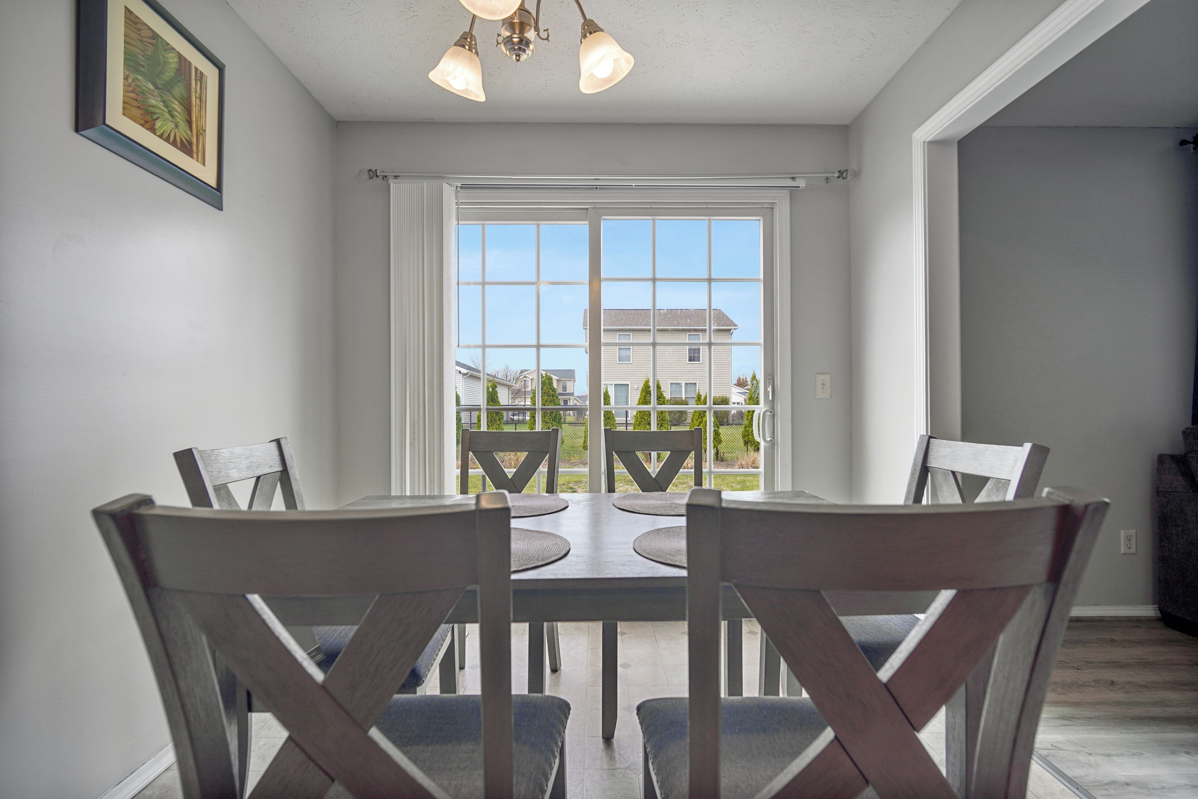 A dining area with a table and chairs, a window with a view of houses, and a ceiling light fixture.