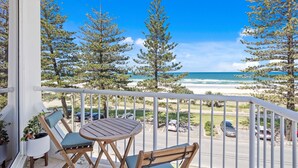 A balcony with a wooden table and two chairs, overlooking a beach with snow-covered trees and a clear blue sky. - Amazing Beachfront Escape (Miami)