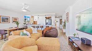 A modern living room with a large sectional sofa, a dining area with a wooden table, and a kitchen in the background. - Amazing Beachfront Escape (Miami)