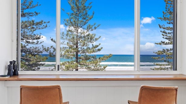A room with a large window overlooking a beach and trees. There are two chairs in the room. - Amazing Beachfront Escape (Miami)