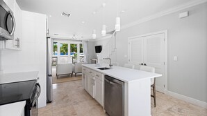 Een moderne keuken met witte kasten, een centraal eiland, roestvrijstalen apparatuur en hanglampen.