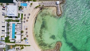 Eine Luftaufnahme eines Strandraises mit Schwimmbad, Liegestühlen und felsiger Küstenlinie.
