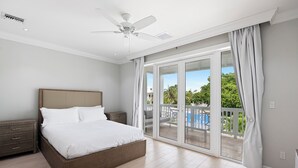Een slaapkamer met een groot bed, een plafondventilator en een schuifdeur naar een balkon met een zwembad.