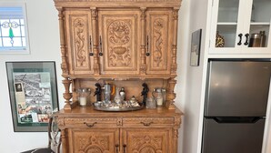 Ein Holzschrank mit aufwendigen Schnitzereien, ein Edelstahlkühlschrank und eine gerahmte Karte an der Wand.