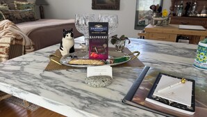 Eine Marmor-Küchenarbeitsplatte mit einer Schokoladenschachtel, einer Katzenfigur, einem Glas und einem Notizbuch.