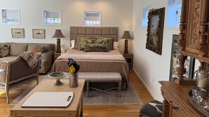 Ein helles Schlafzimmer mit einem großen Bett, Nachttischlampen, einer Holzkommode und einem Essbereich mit Tisch und Stühlen.