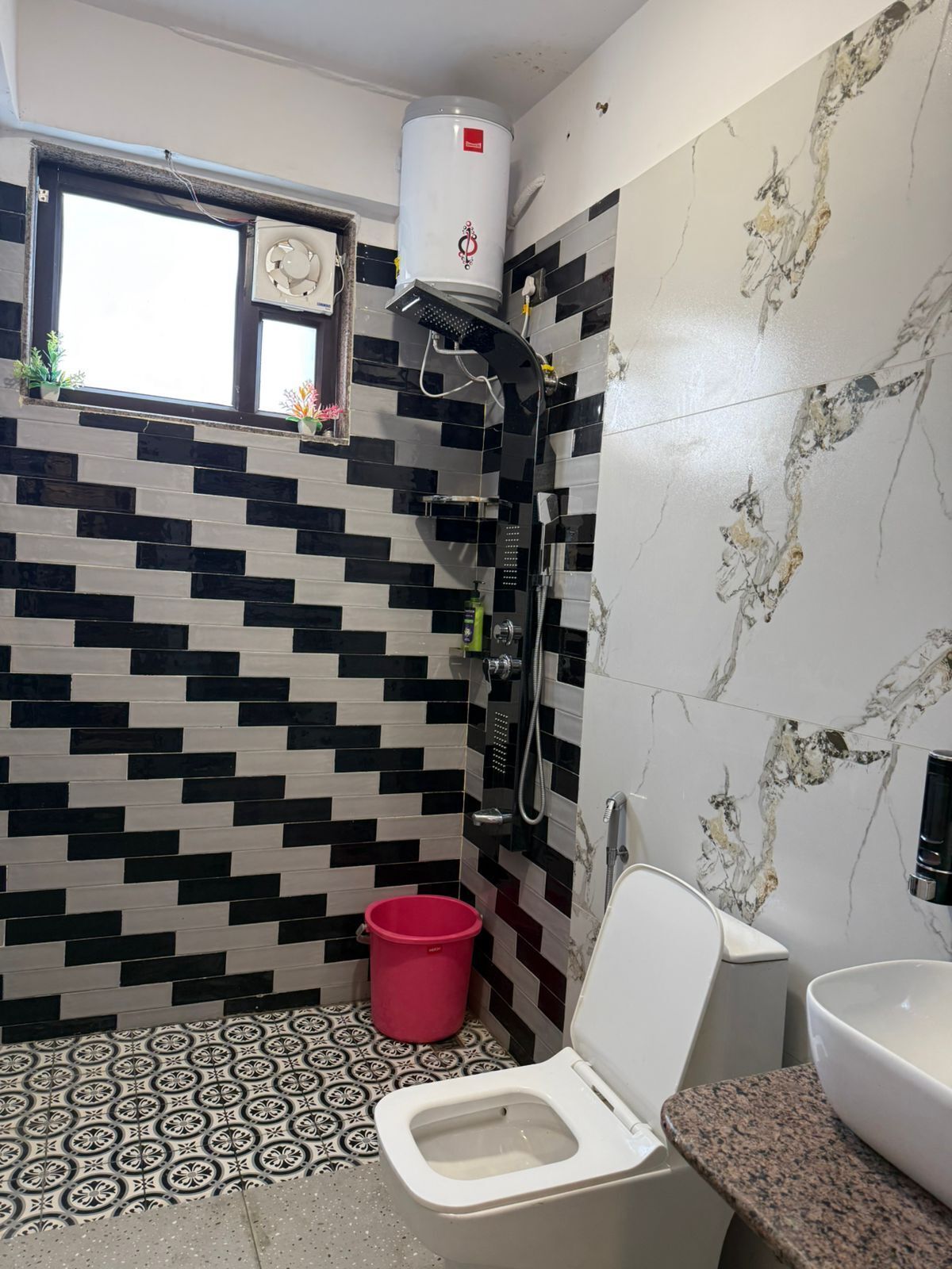 Casa de banho com parede revestida a azulejos preto e branco, chuveiro, sanita e lavatório.