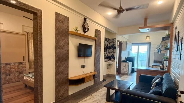 A modern living room with a dark sofa, a flat-screen TV mounted on a wall, a ceiling fan, and a marble-patterned floor. - Hotel Sacred Roots (Rishikesh)