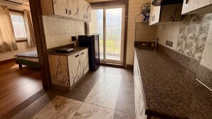 A kitchen with marble cabinets, a granite countertop, and a sliding glass door leading to a balcony. - Hotel Sacred Roots (Rishikesh)