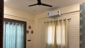 A hotel room with a bed, a ceiling fan, an air conditioning unit, and a window with curtains. - Hotel Sacred Roots (Rishikesh)
