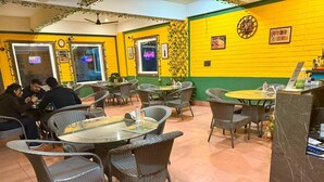 A restaurant with wicker chairs and tables, yellow and green walls, and a clock on the wall. - Hotel Sacred Roots (Rishikesh)