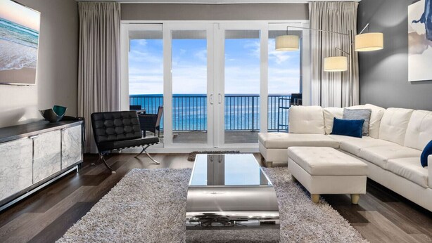 Een moderne woonkamer met een groot raam met uitzicht op de zee, een witte bank, een zwarte fauteuil en een marmeren kast.