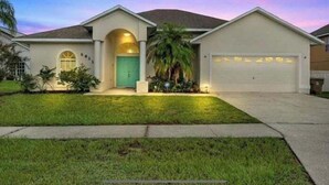 A single-story house with a green door, a garage, and a well-maintained lawn. - 5BR Disney Retreat | Private Pool, Spa & Game Room — Sleeps 14 (Kissimmee)
