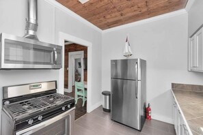 A modern kitchen with a stainless steel stove, microwave, and refrigerator, a wooden ceiling, and a tiled floor. - Adorable 1-bedroom house w/private entrance, beach 2 blks in charming Galveston (Galveston)