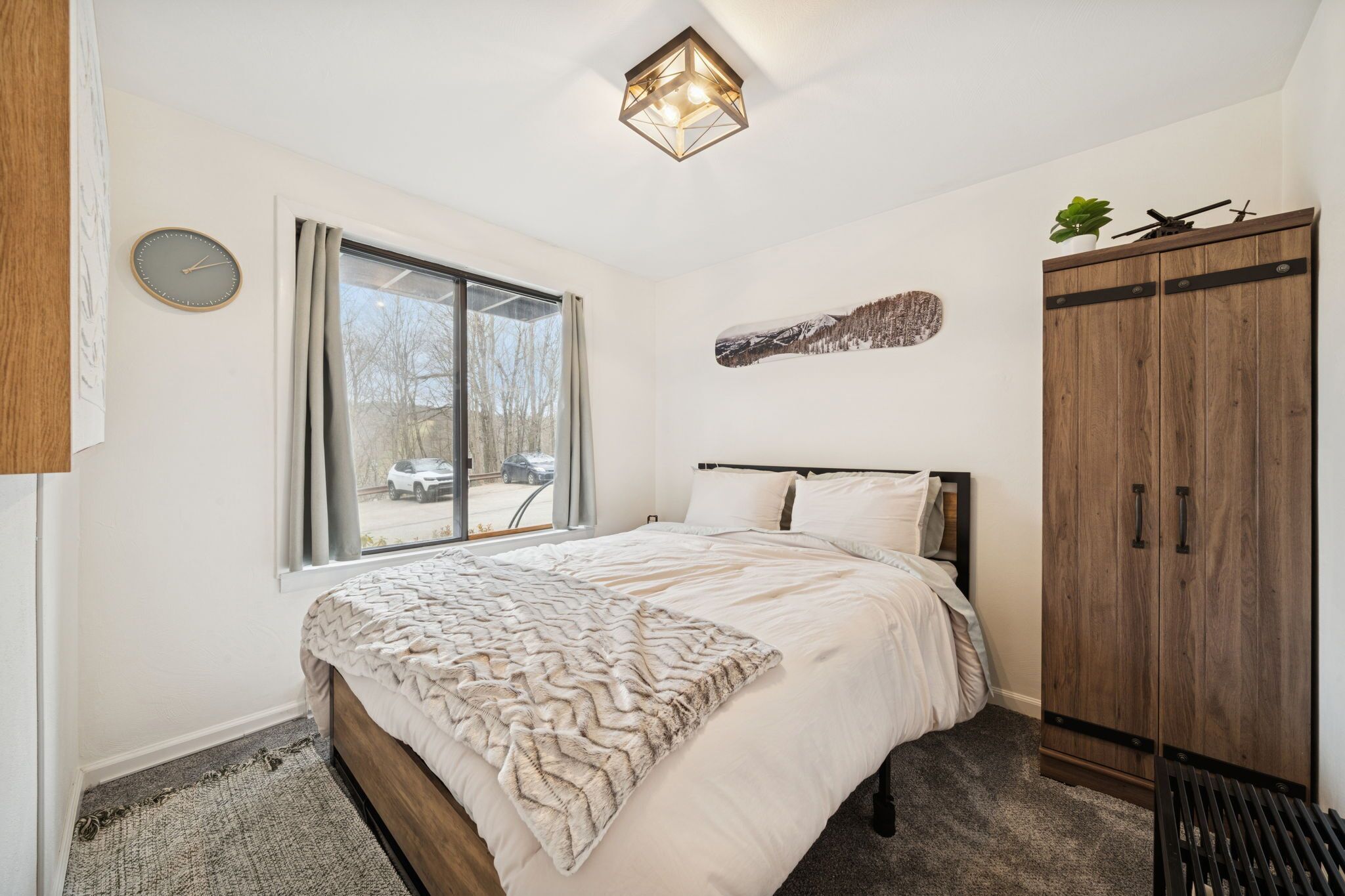 Ein Schlafzimmer mit Bett, Fenster, Kleiderschrank und Wanduhr.