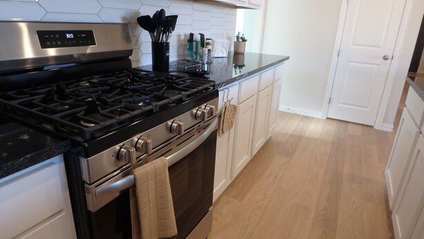 Une cuisine équipée d’une cuisinière en acier inoxydable, de meubles blancs et d’un plancher en bois.