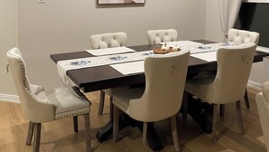 Un coin repas comprenant une table rectangulaire, six chaises blanches à revêtement rembourré et un tableau abstrait encadré accroché au mur.