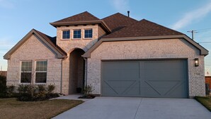 Une maison à deux étages avec une façade en briques, un garage et un ciel dégagé.