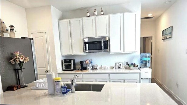 Cozinha moderna com armários brancos, uma ilha central, micro-ondas e cafeteira.