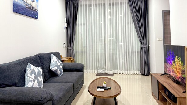 Una sala moderna con un sofá gris oscuro, una mesita de centro de madera y un televisor sobre un mueble de madera.