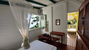 A room with a bed, a small table, a desk, a window with a green frame, and a door leading to an outdoor area. - Villa, lodge 6-7 pers, exceptional view, comfort and nature from the center. (Le Diamant)