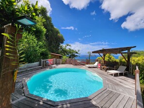 A wooden deck with a swimming pool, surrounded by greenery and a wooden fence. - Villa, lodge 6-7 pers, exceptional view, comfort and nature from the center. (Le Diamant)